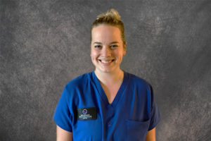 nurse with hair in a bun wearing blue scrubs against a gray background